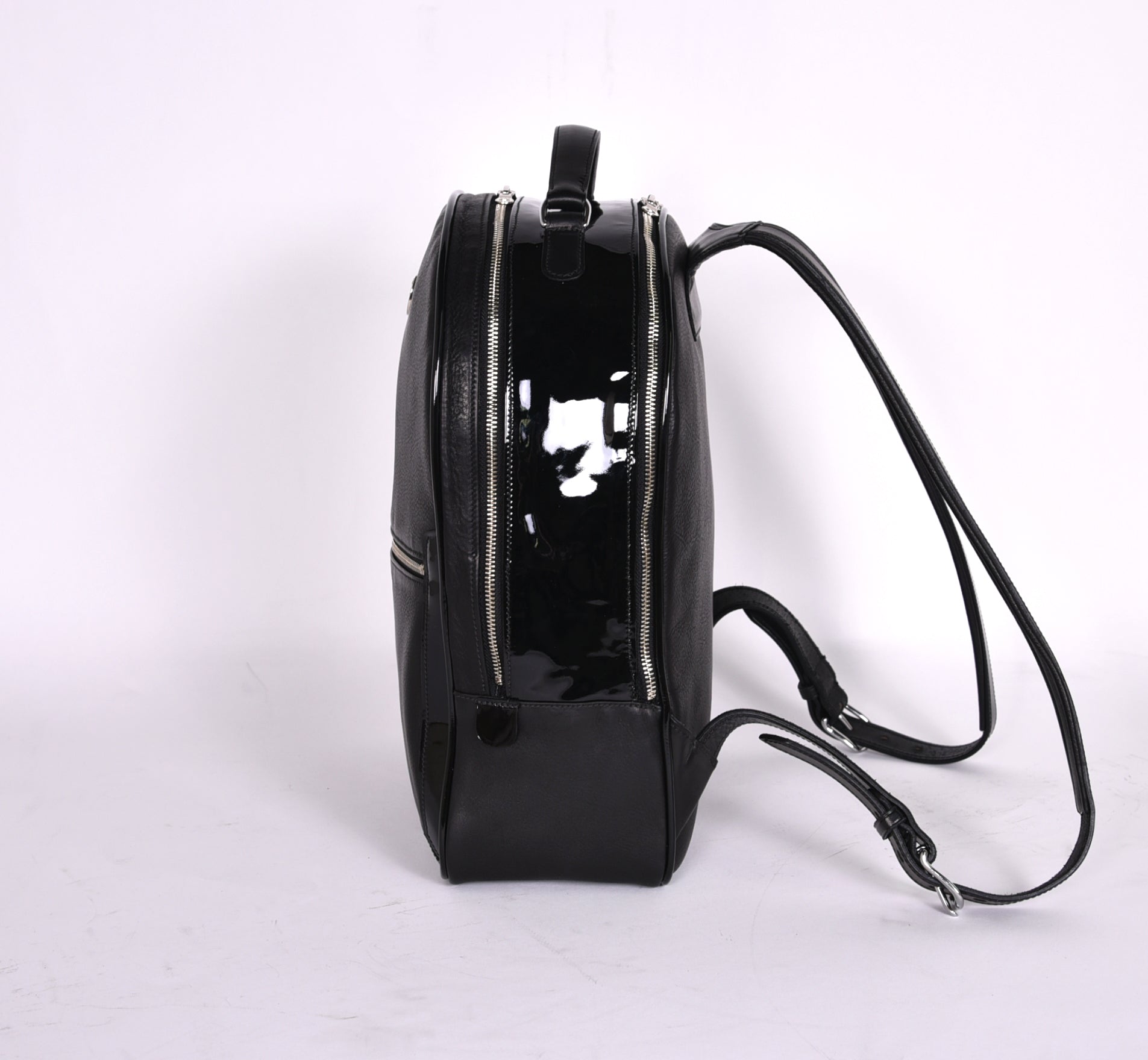 Black leather backpack, The Jaunty by Freedman's, side profile with patent leather panel, zippers, and shoulder straps.