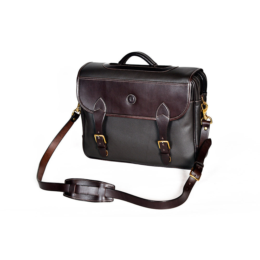 Wagonette Briefcase, dark brown textured leather, flap closure with dual buckle straps, silver hardware, contrast stitching, embossed circular logo on front, detachable shoulder strap with padded section, white background.