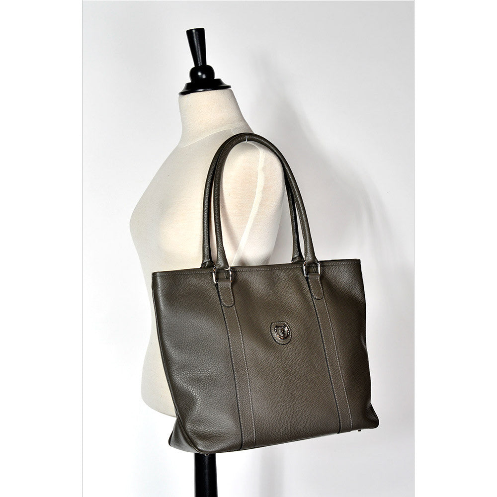 reedman's Victoria Tote, grey textured leather, high gloss patent leather handles, silver circular logo on front, light contrast stitching, light background.
