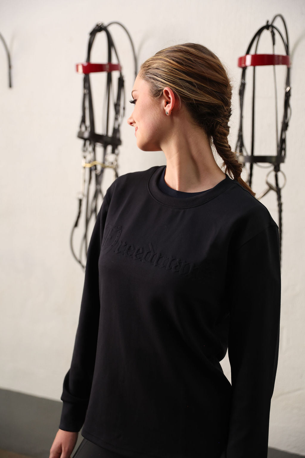 Women wearing a black sweatshirt with Freedman text, standing in front of equestrian equipment.