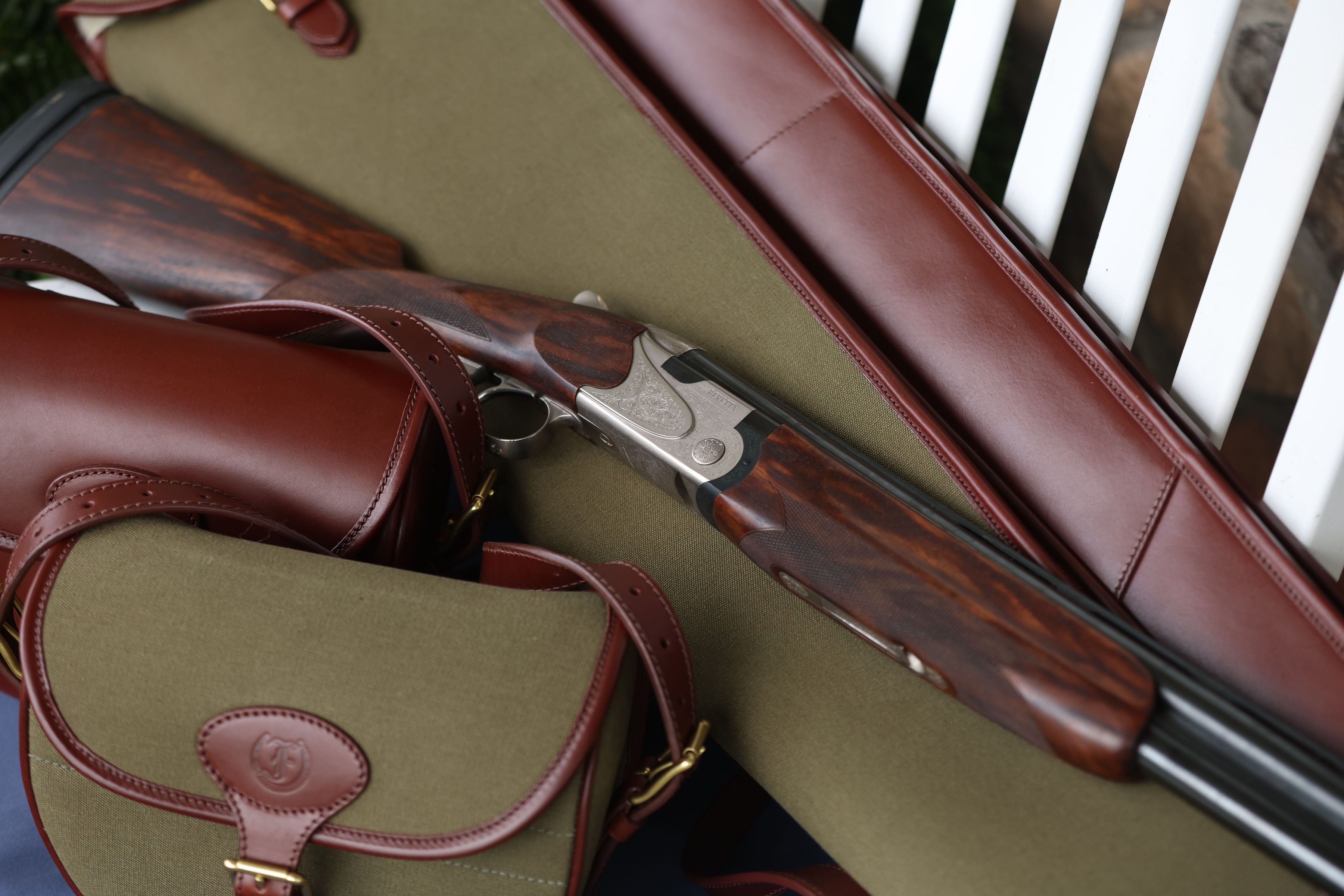 Over-under shotgun resting on a Military Green Sandringham Gun Slip with Havana brown leather trim, outdoors on a wooden surface, made by Freedman’s Harness.