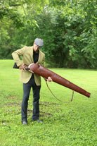 Man wearing a green tweed jacket and cap holding a Havana Brown Leather Sandringham Gun Slip outdoors on a grassy field, made by Freedman’s Harness.