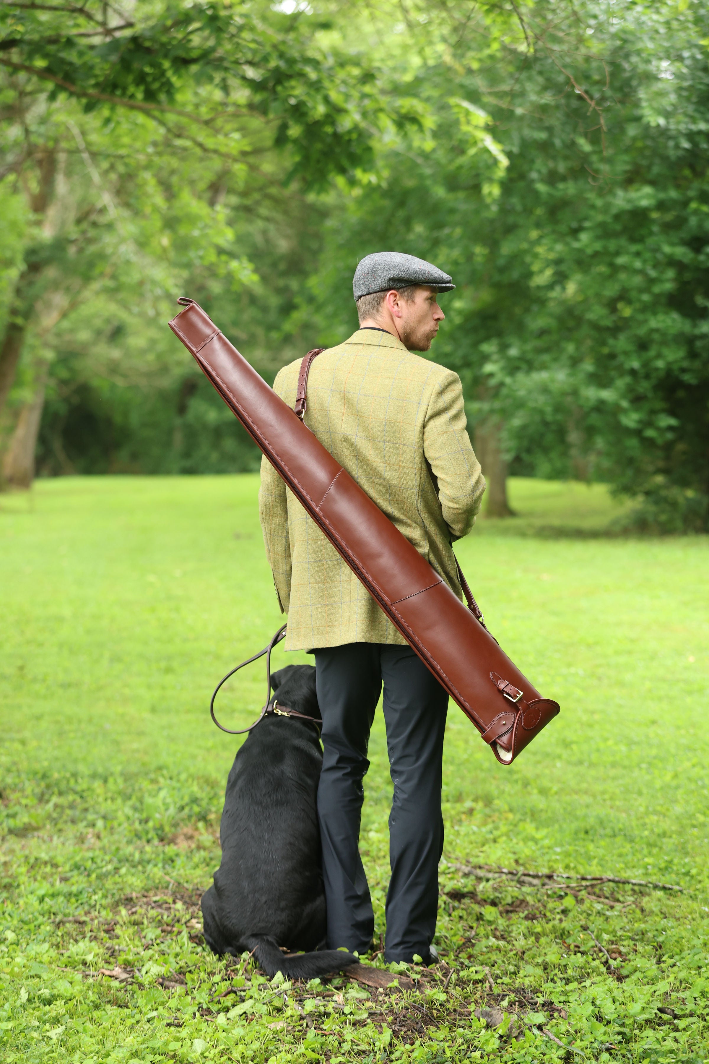 Man holding a Havana Brown Leather Sandringham Gun Slip with a dog in a grassy outdoor setting, made by Freedman’s Harness.