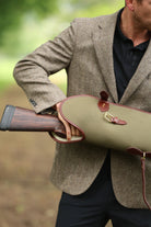 Man in a brown tweed jacket holding a Military Green Sandringham Gun Slip with Havana brown leather trim in an outdoor setting, made by Freedman’s Harness.