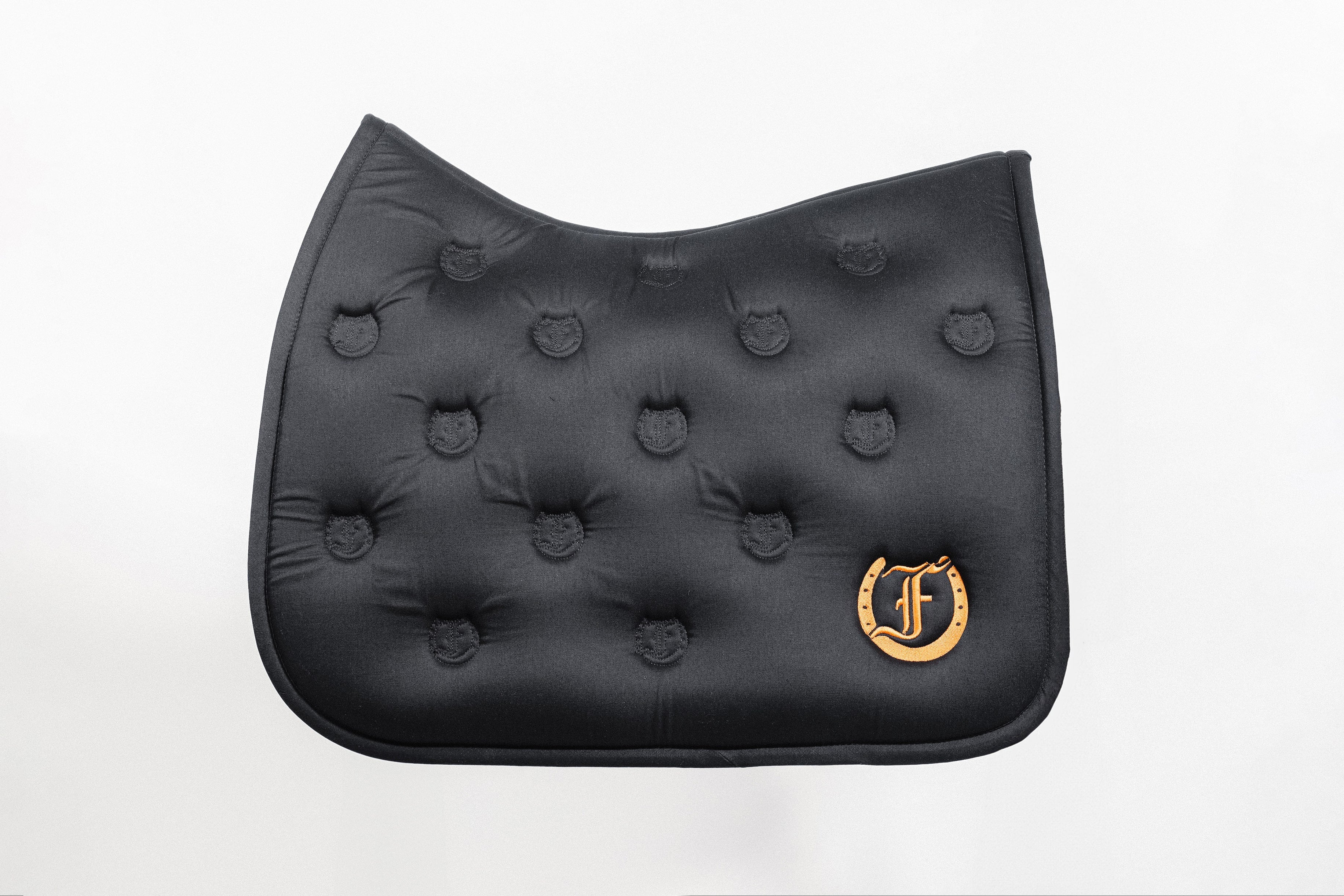 Black quilted saddle pad with a soft and absorbent bamboo lining, featuring an embroidered Freedman's logo, shown on a white background