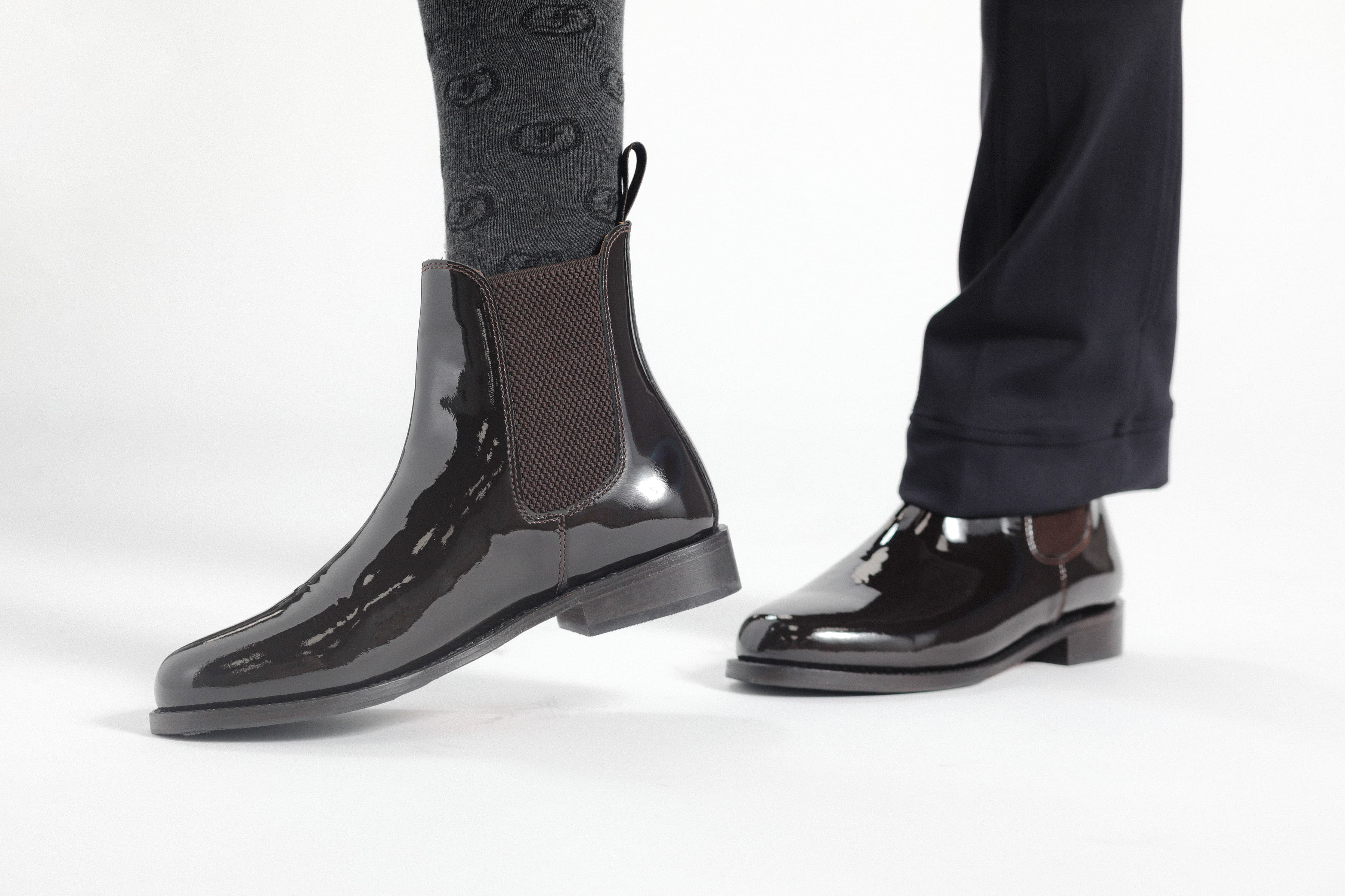  Pair of black patent leather Adelaide Show Jodhpur Boots on a person's feet, with patterned socks visible