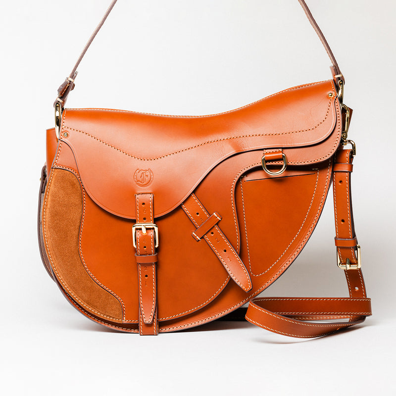 Freedman’s Burghley Shoulder Bag in cognac leather, featuring gold finished hardware, a distinctive saddle-inspired silhouette, and an adjustable shoulder strap, on a white background. 