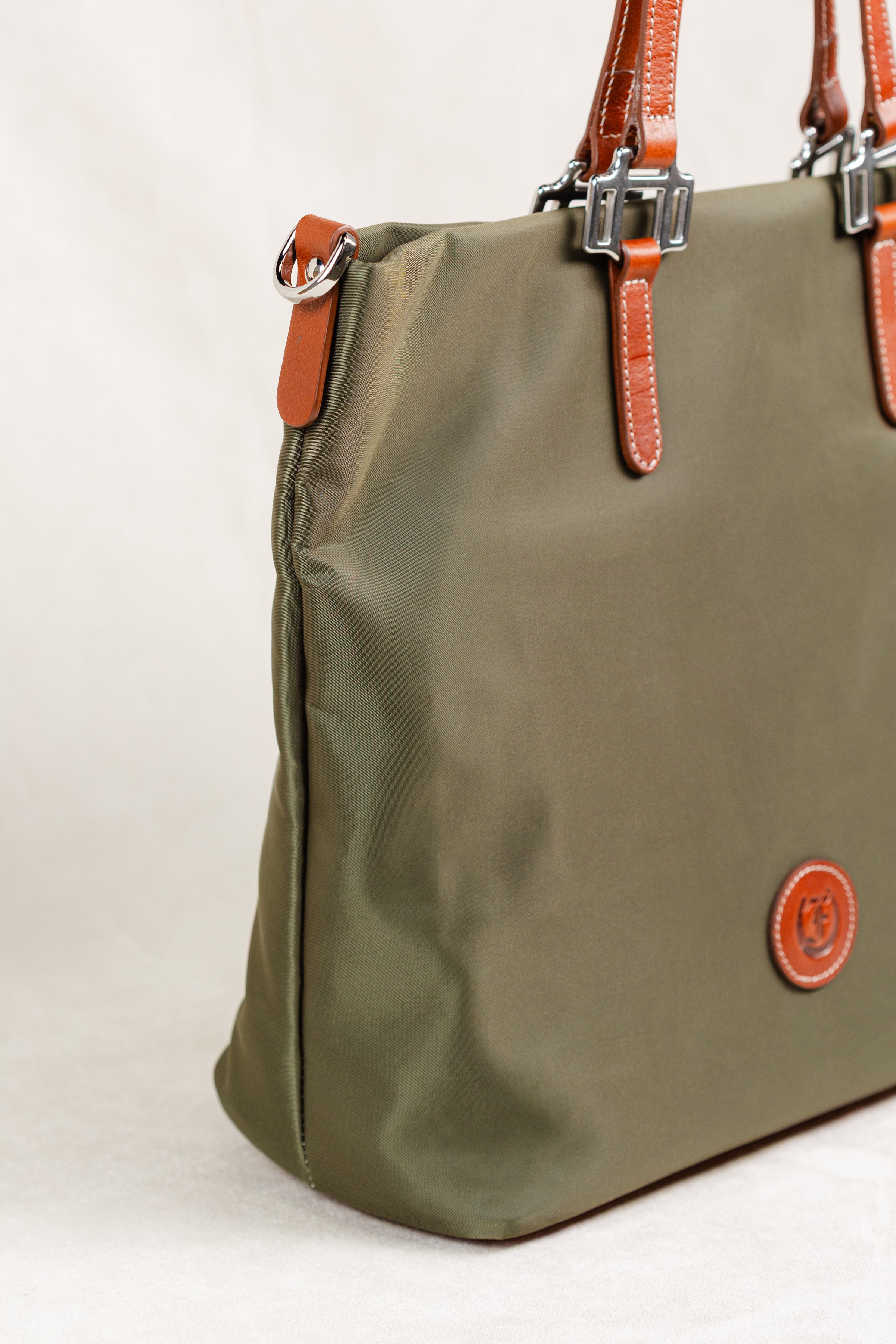 Freedman's Conestoga Tote in olive green, detailed side view showcasing the bag's shape, texture, brown leather handles with silver hardware, and the brand's circular logo patch.