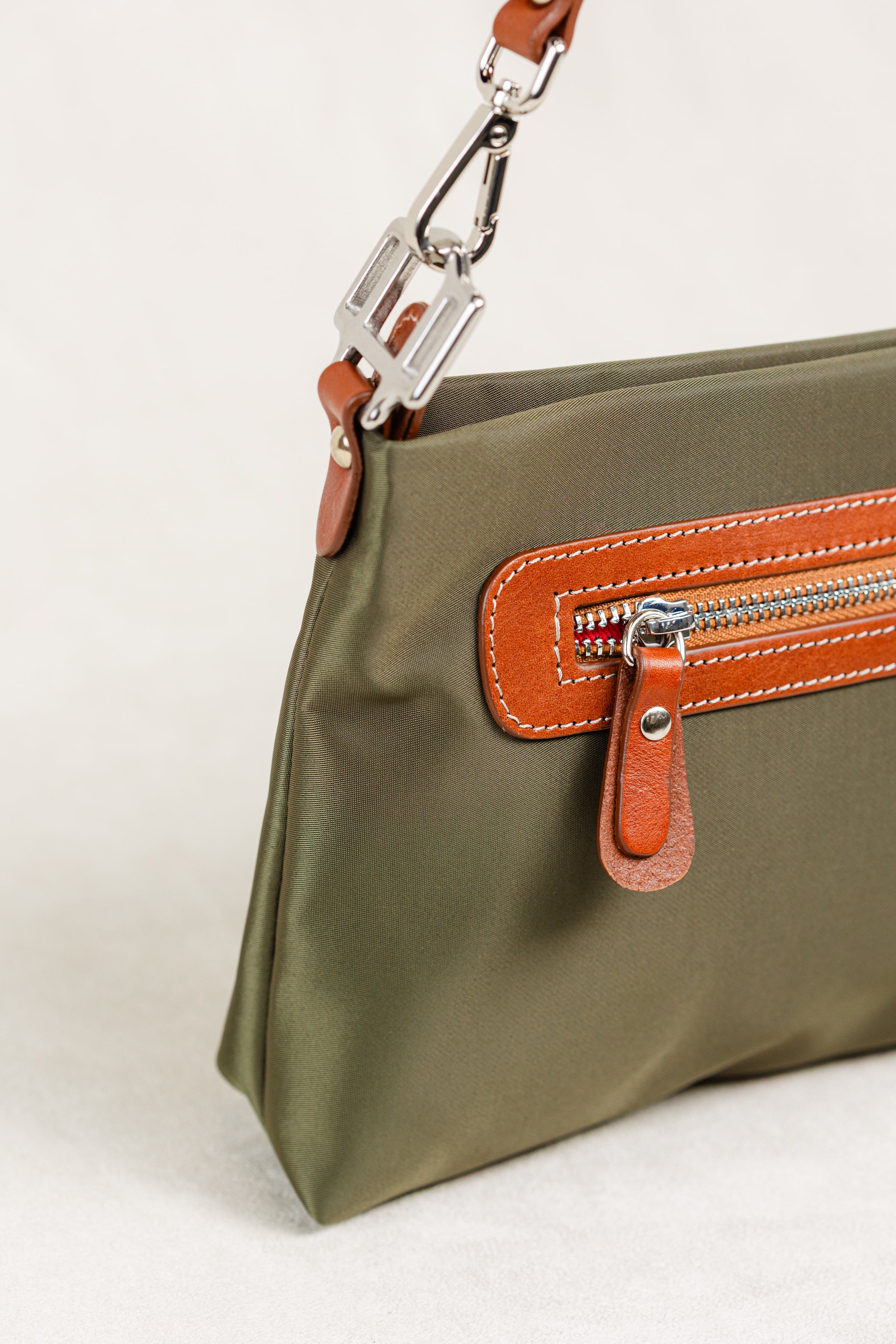 Freedman's Dokar Bag in olive green, detail shot showing the silver hardware clasp, brown leather strap, and the front zipper pocket with brown leather and red zipper teeth.