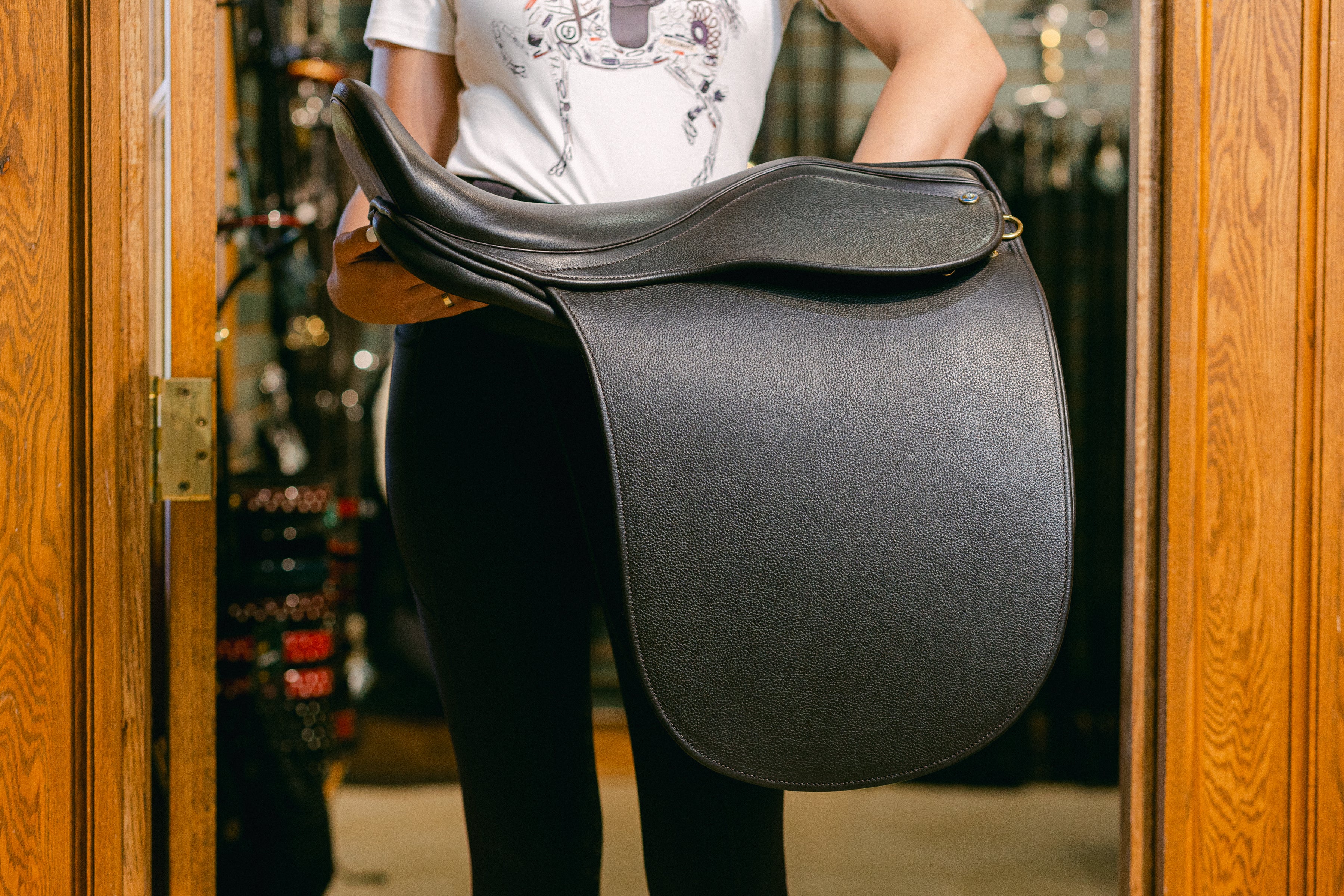 Freedman’s Ultra XD Saddle cutback saddle with a deep seat for a secure riding experience, shown in black leather and held by a rider in a tack shop doorway.