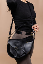 A woman in a black top and dark pants holds the Freedman's Burghley Shoulder Bag on her shoulder.
