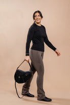 A woman in a black top and brown leggings walks while holding the Freedman's Burghley Shoulder Bag.