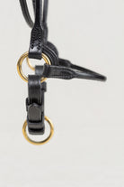 Close-up of a black leather strap or bridle component with gold-tone metal rings, shown against a plain light background.