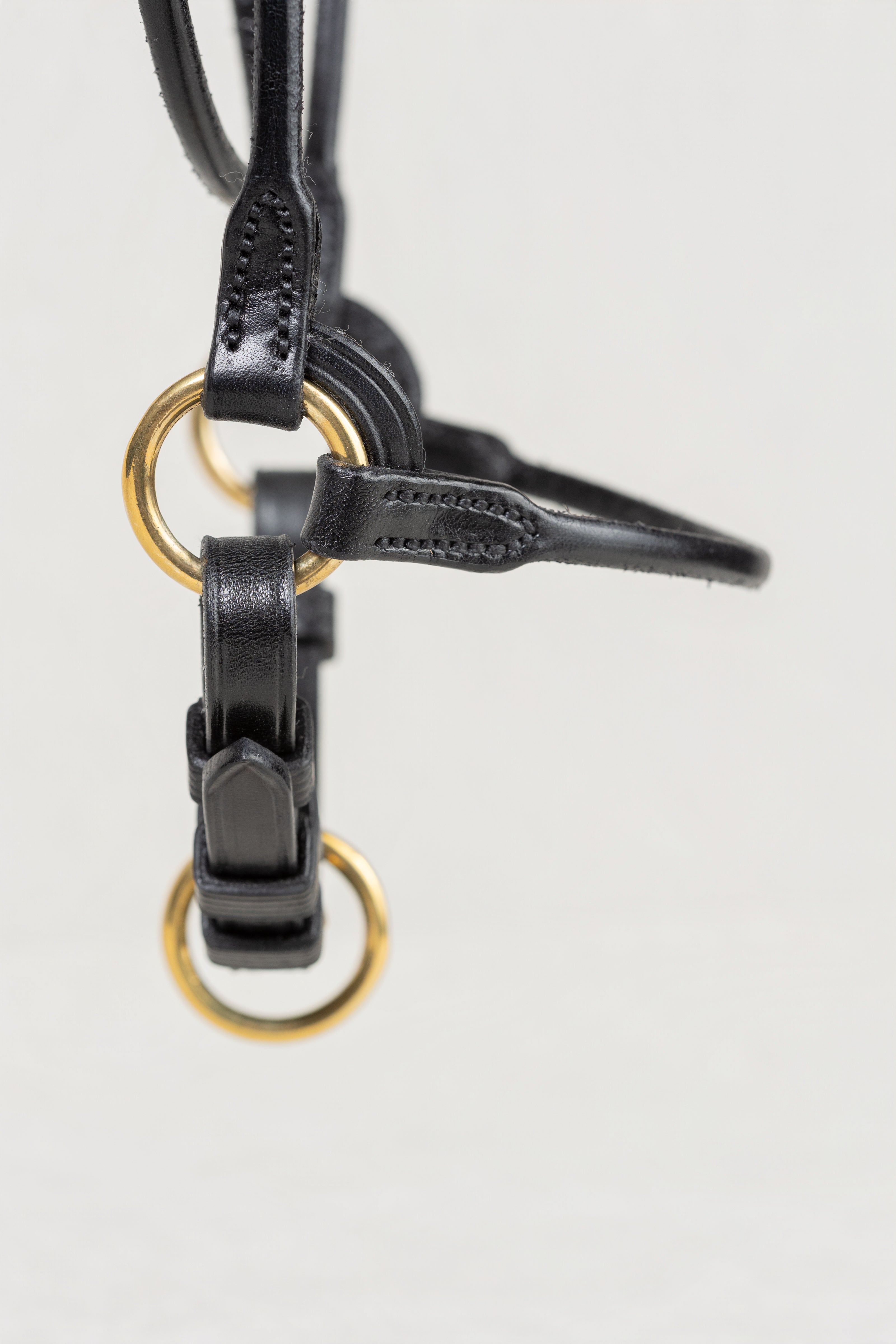 Close-up of a black leather strap or bridle component with gold-tone metal rings, shown against a plain light background.