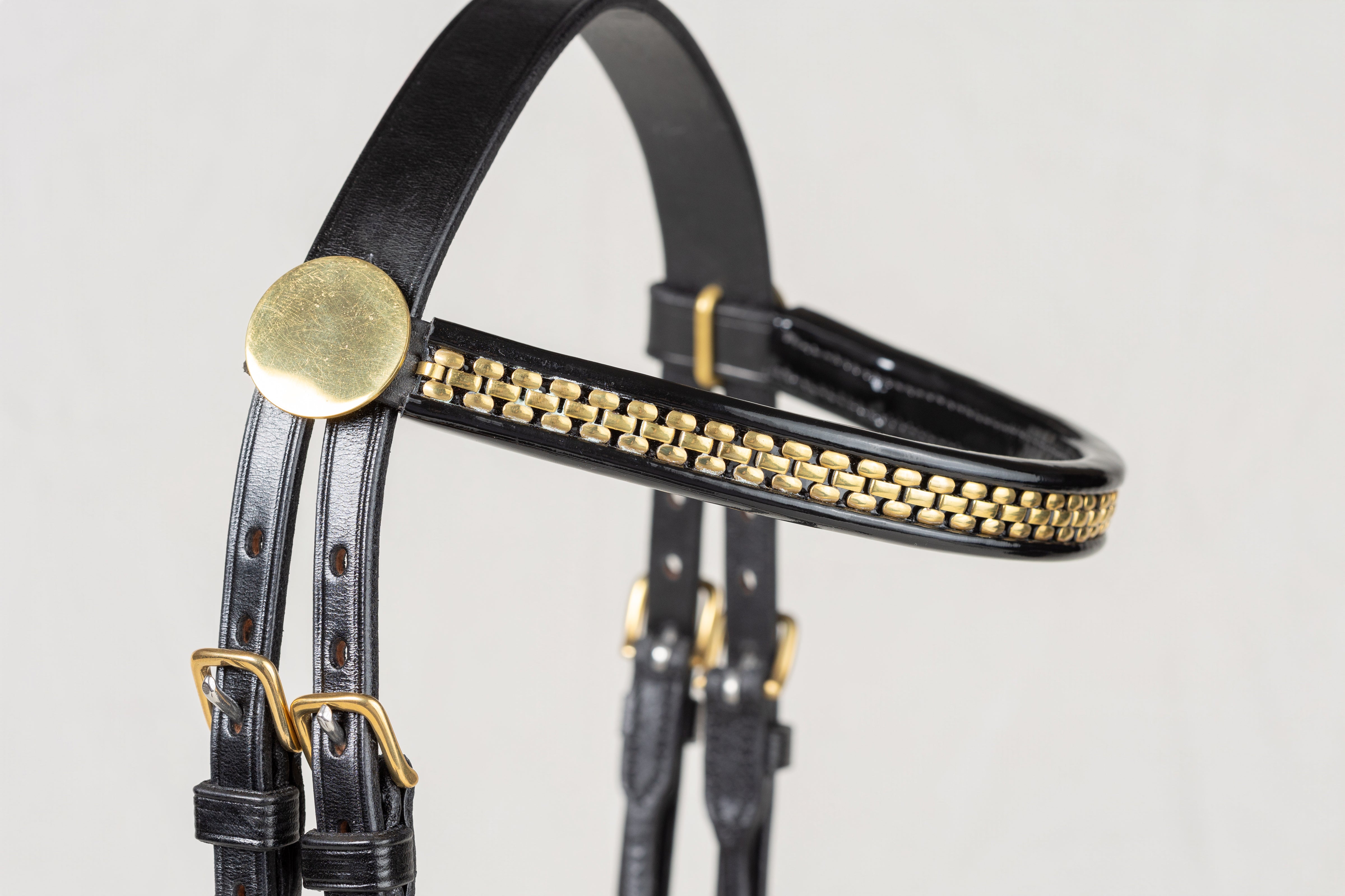 Black leather horse bridle headpiece with gold-tone chain detailing and brass buckles, shown against a light gray background.