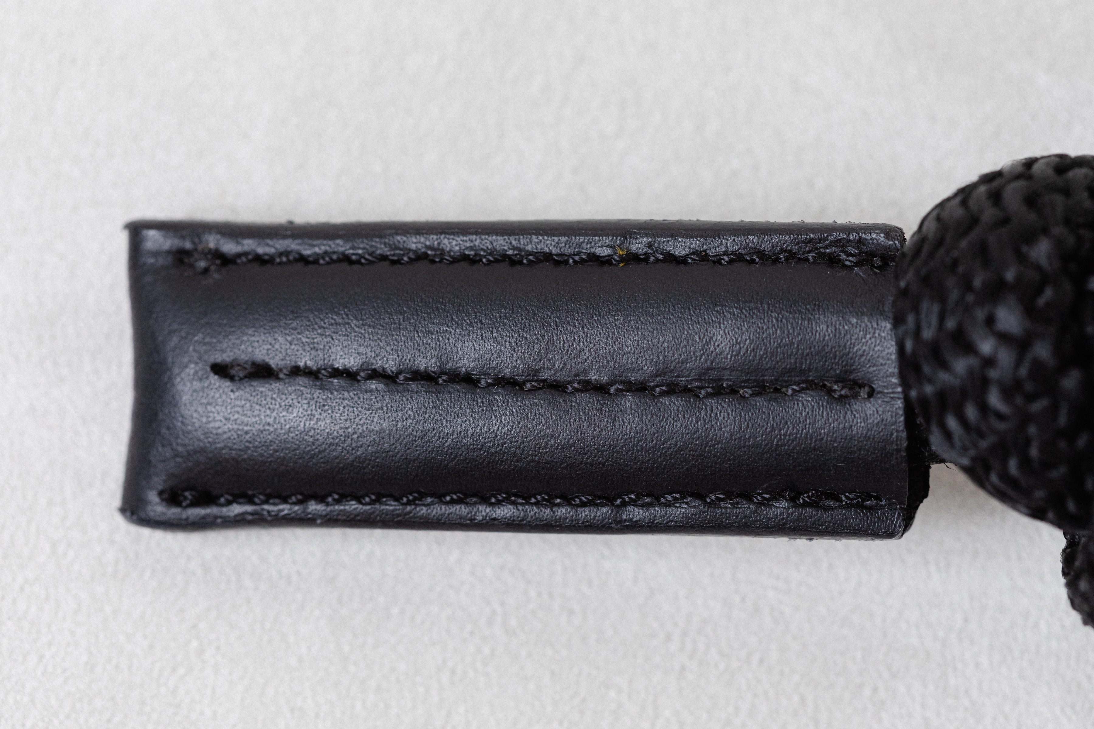 Close-up of a black leather strap with stitching on a light gray background