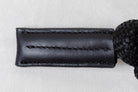Close-up of a black leather strap with stitching on a light gray background