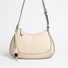 Carlisle Bag in putty leather by Freedman Harness – elegant crossbody handbag with gold hardware, adjustable strap, and minimalist curved silhouette