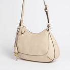 Side view of Carlisle Bag in putty leather by Freedman Harness – structured crossbody bag with gold logo charm, curved silhouette, and adjustable strap
