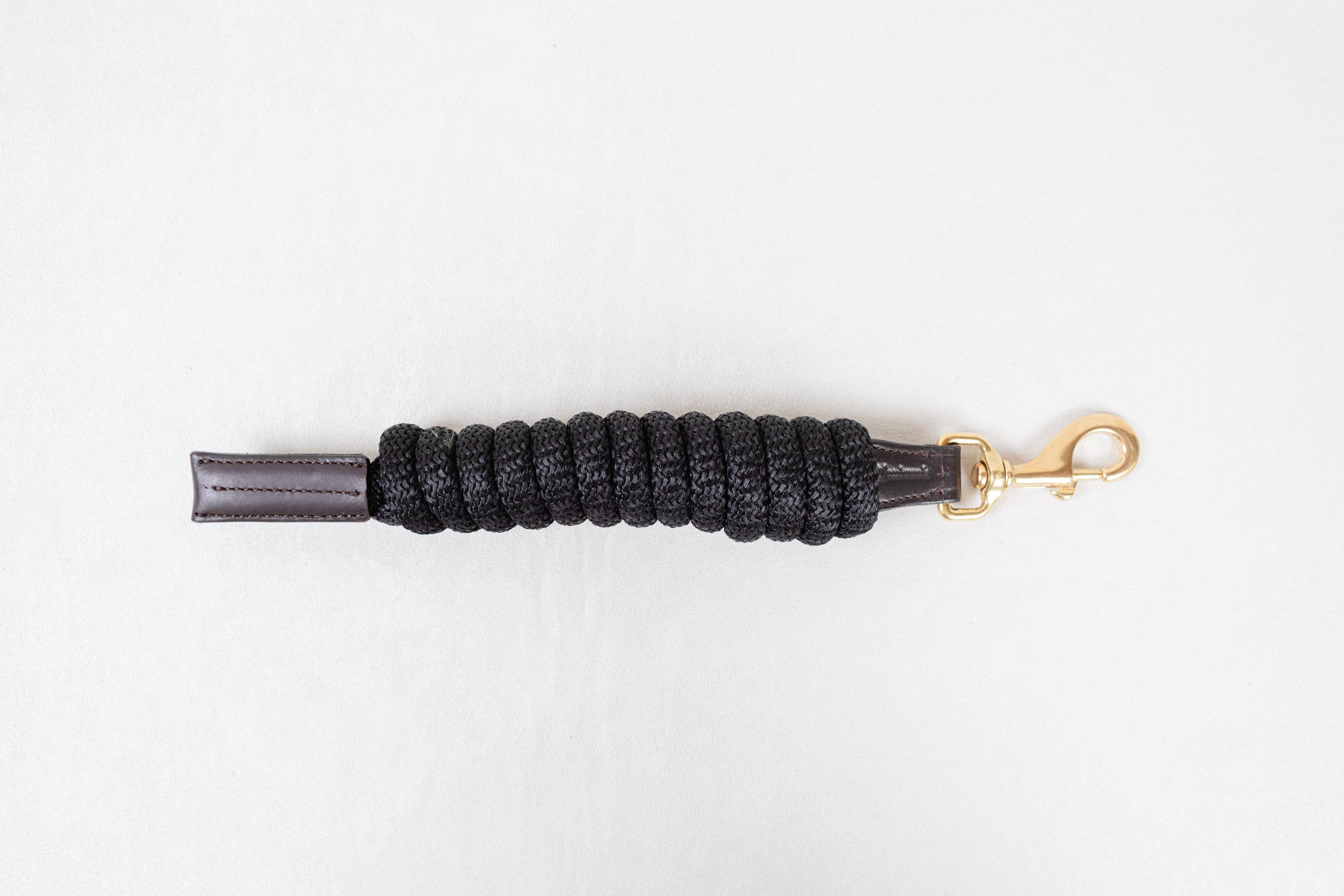Freedman Harness black paracord poly lead rope with premium brown leather accents and a brass snap on a white background.