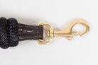 Detailed close-up of the brass snap hook on a Freedman Harness black lead rope, showing the spring-loaded mechanism and the rich texture of the brown leather wrap on a white background