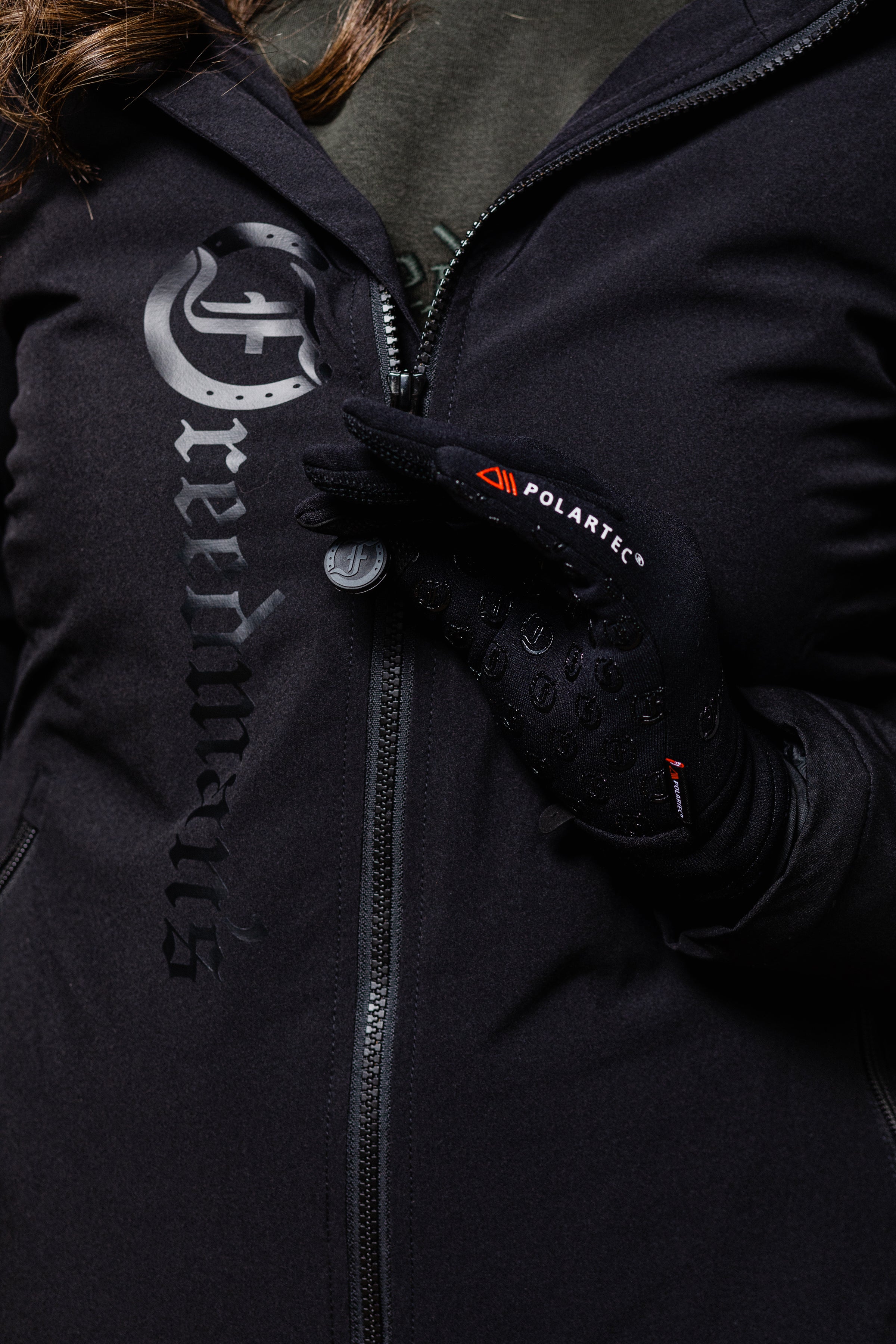 Close-up of a person wearing a black Freedman's jacket with a large logo and black Polartec gloves with visible logo.