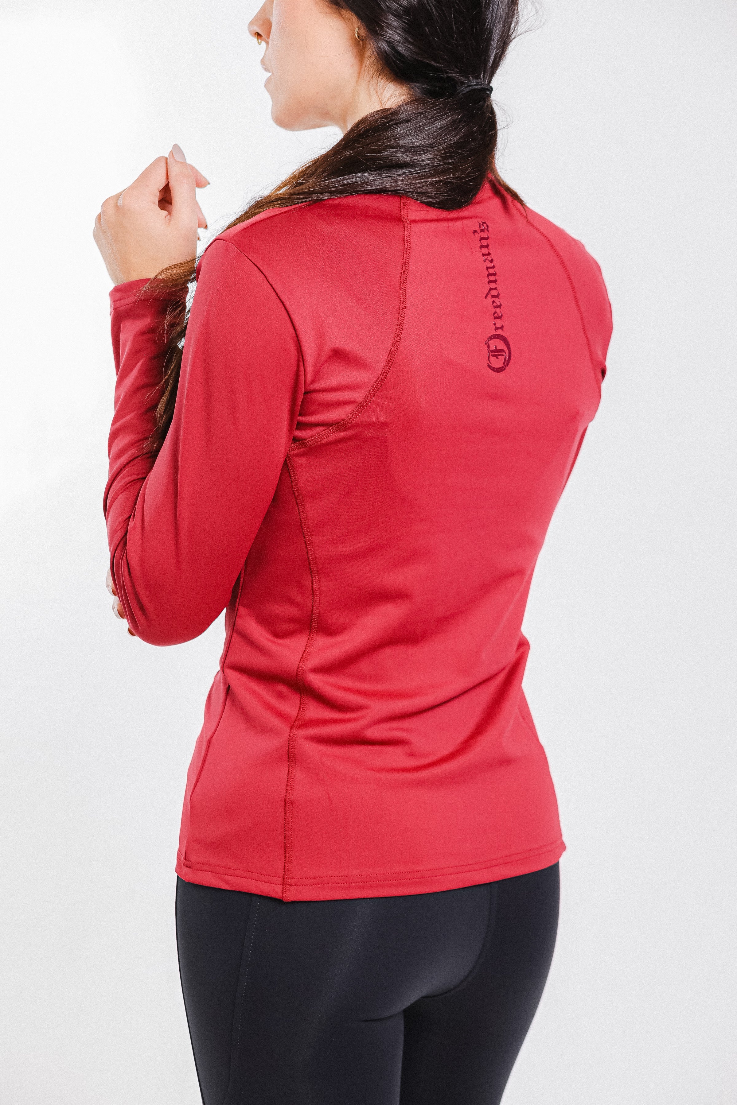 Back view of a woman wearing the Tess Ladies' 1/4 Zip Long Sleeve Top by Freedman's in vibrant red, showcasing the Freedman's logo and stylish performance design for equestrian and activewear use