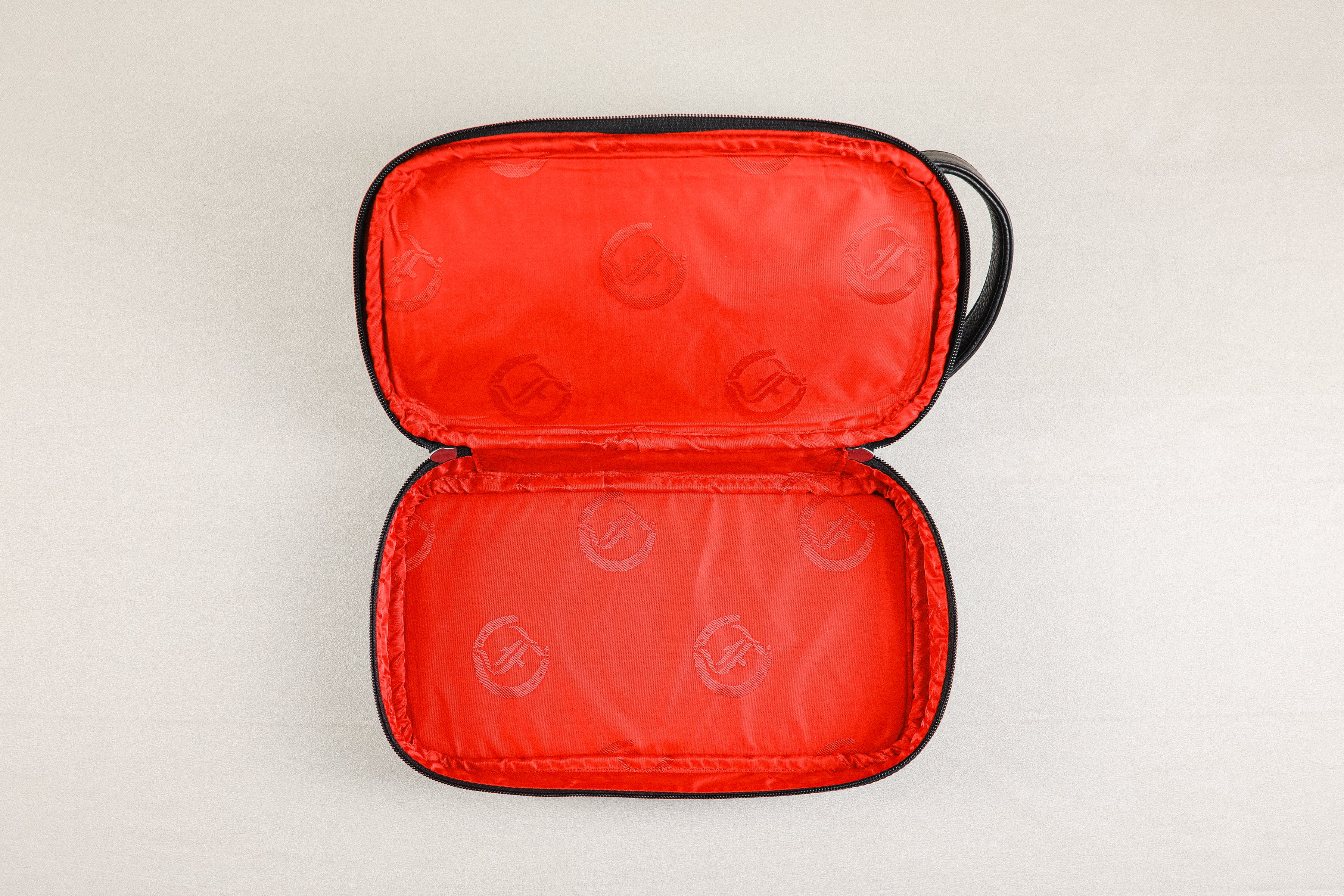 op-down view of open Freedman's Cardiff Shave Bag, black leather exterior visible, bright red fabric lining in both compartments with repeated embossed Freedman's "F" logo pattern, open zipper, light background.