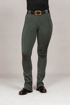 Front view of women's Umber Green jodhpurs by Freedman Harness, featuring full seat silicone grip, flared leg, brown belt with gold buckle, and black riding boots – high-performance equestrian pant