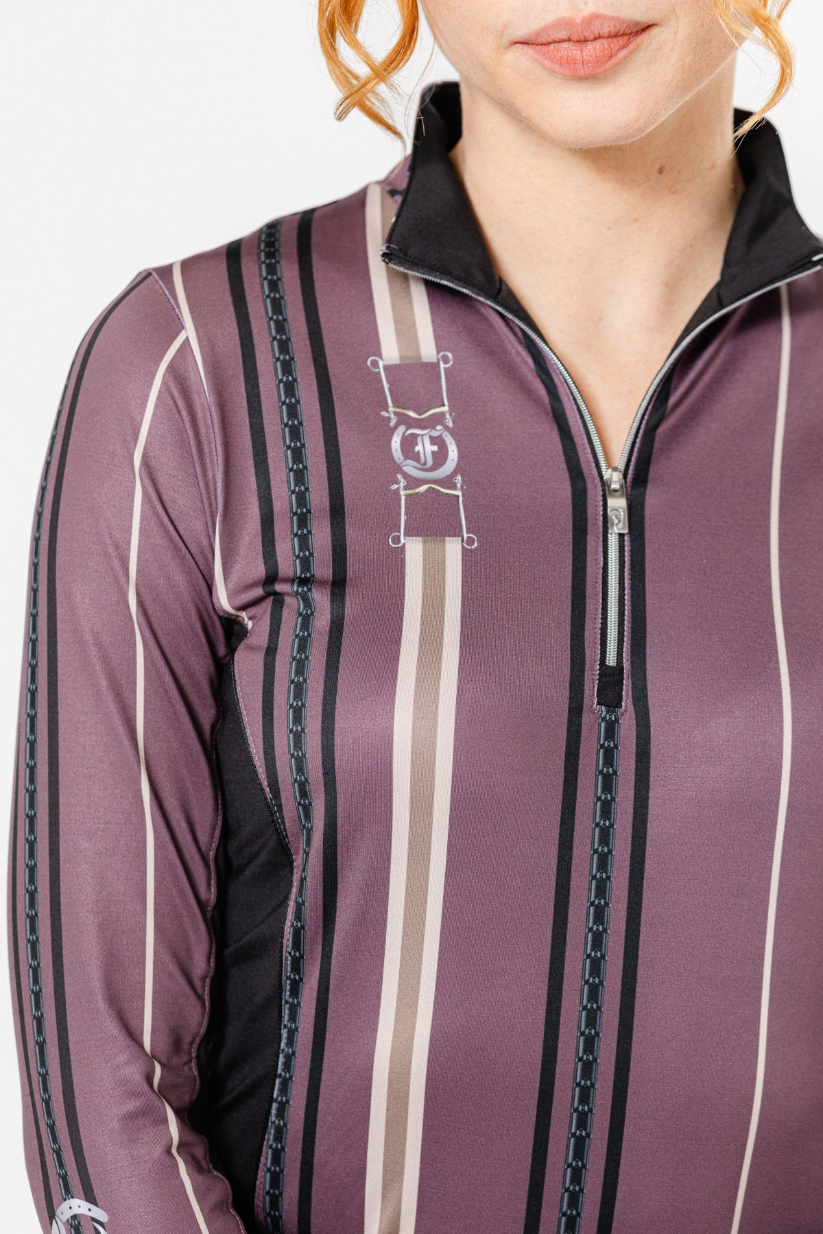 A close-up of a woman wearing the Nancy 1/4 Zip Long Sleeve Shirt by Freedman’s, featuring a stylish striped pattern in shades of purple, black, and beige with equestrian-inspired bit and bridle details. The shirt has a zip-up collar and a sleek, form-fitting design.