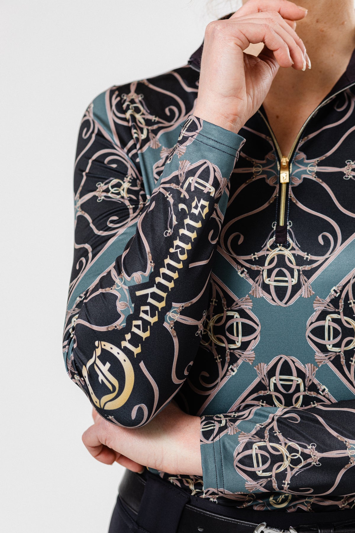 Women wearing the Fantasy 1/4 Zip Long Sleeve Shirt in Black/Forest print. Stylish equestrian-inspired performance top with an intricate geometric pattern, perfect for active and casual wear. Close up of the Freedman's printed logo