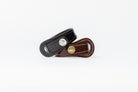 Pair of Signature Leather Bracelets by Freedman's, one black with silver logo button and one brown with brass logo button, both with white stitching, displayed on a white background.