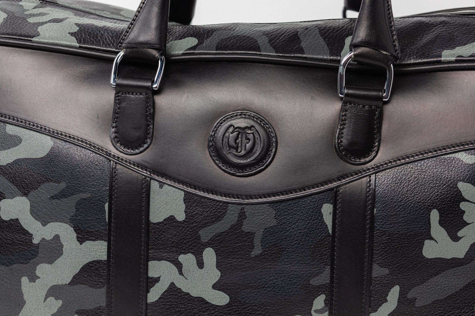 Close-up of camouflage leather overnight bag, The Stanhope by Freedman's, showing embossed logo, handles, and leather texture.
