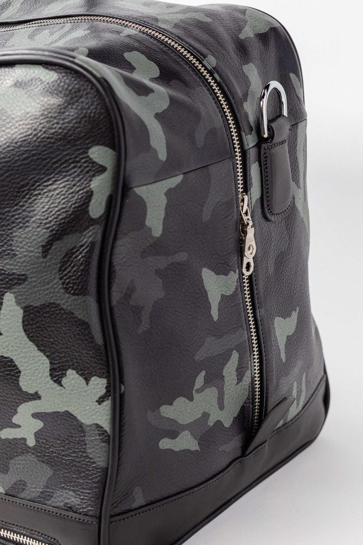 Close-up of Freedman's Grand Break Duffel, camouflage patterned leather, silver zipper with double pulls, silver D-ring hardware, dark leather trim at base, light background.