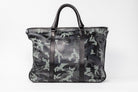 Freedman's Victoria Tote Large, dark textured leather, Camo leather trim along edges and center straps, embossed circular logo on front, light contrast stitching, dual rolled handles with metal hardware, light background.
