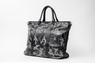 Freedman's Victoria Tote Large, camouflage patterned leather, dark leather trim along edges and center straps, embossed circular logo on front, dual rolled handles, light background.