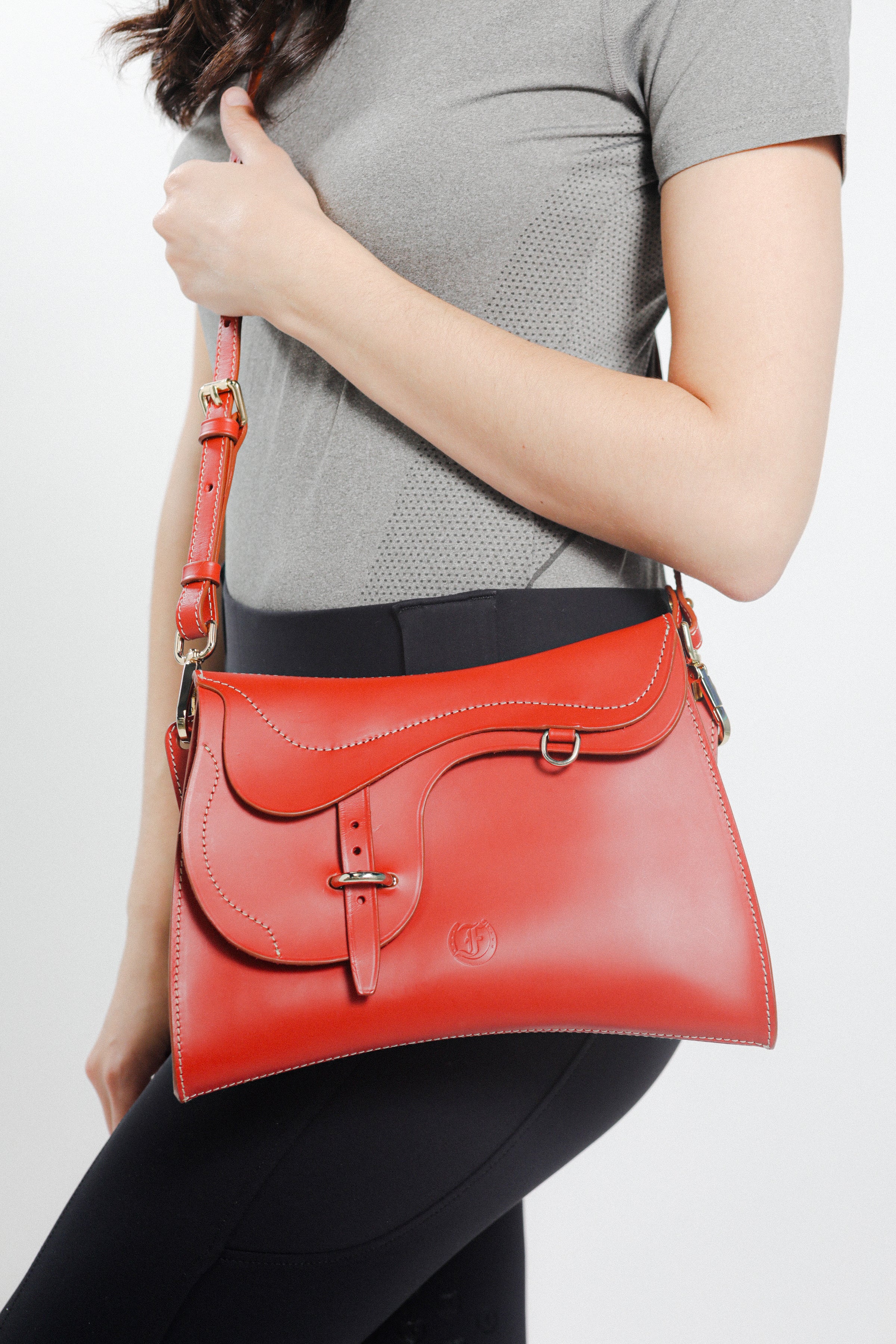 Model carrying Trooper Shoulder Bag in red leather by Freedman Harness – equestrian-inspired crossbody with curved flap, contrast stitching, and gold hardware