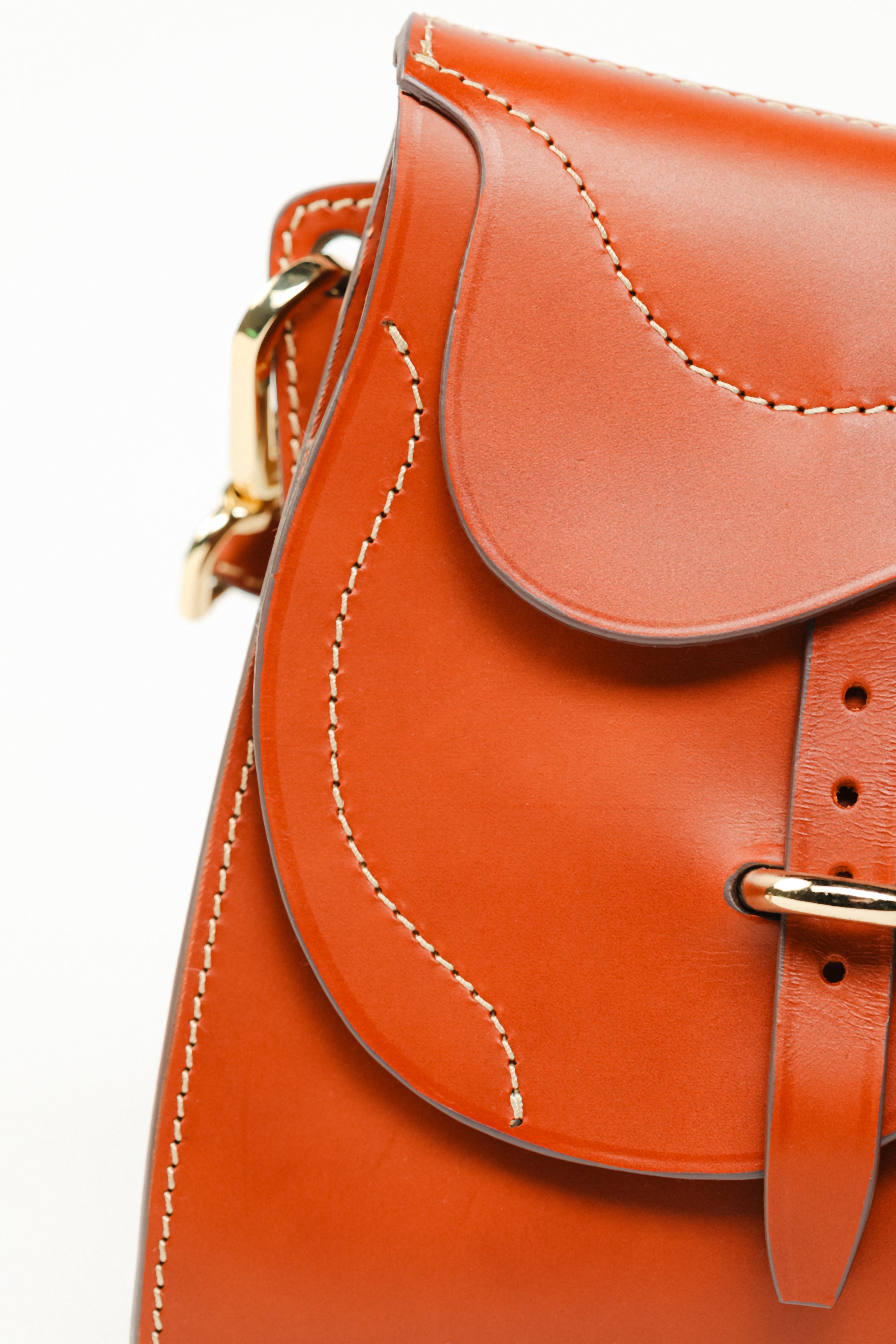 Detail of Trooper Shoulder Bag in cognac leather by Freedman Harness – curved saddle flap with contrast stitching and gold buckle hardware