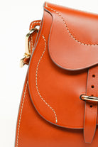 Detail of Trooper Shoulder Bag in cognac leather by Freedman Harness – curved saddle flap with contrast stitching and gold buckle hardware