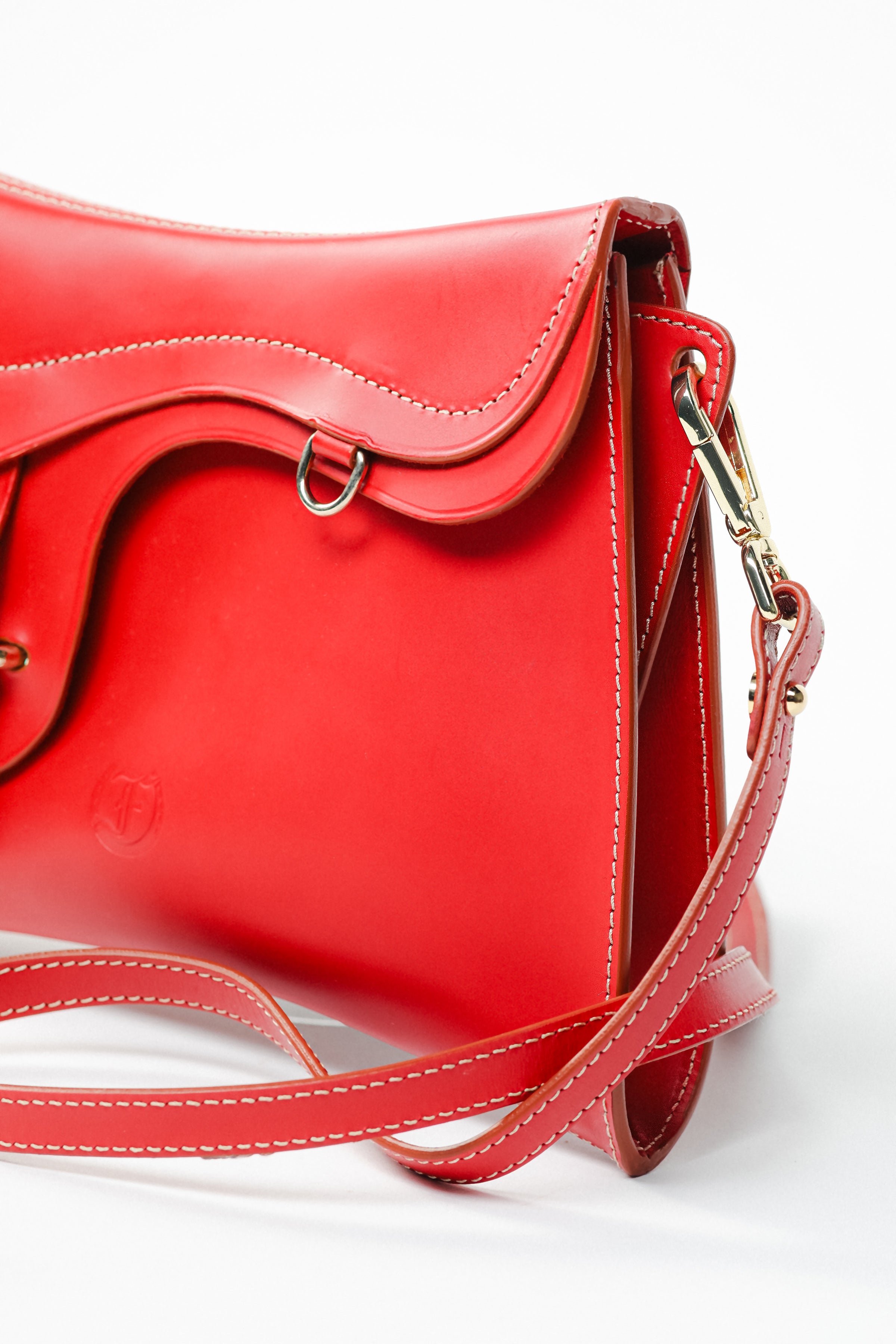 Close-up of Trooper Shoulder Bag in red leather by Freedman Harness – curved flap design, contrast stitching, gold clasp, and embossed logo detail