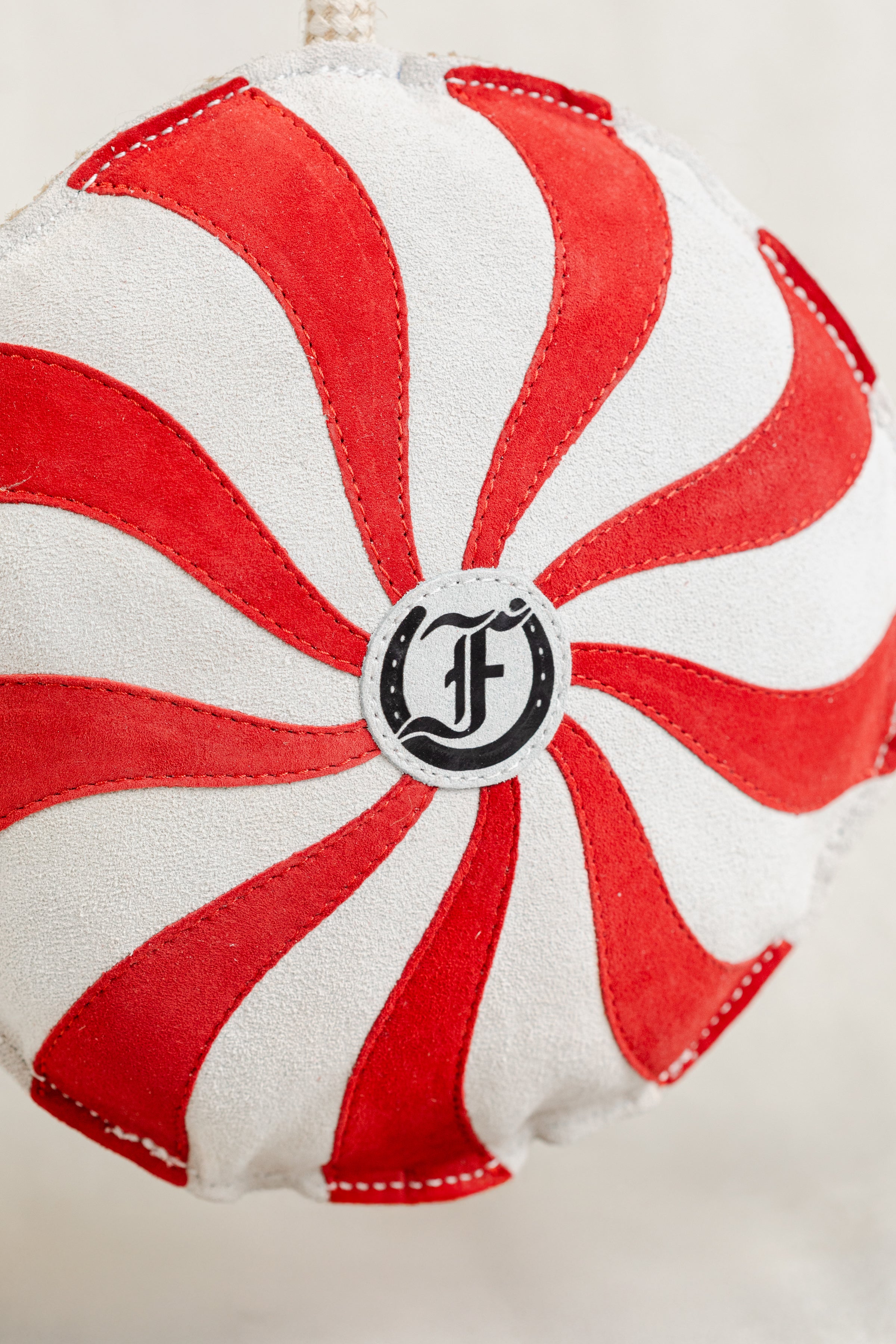 Macro detail of the red-and-white peppermint swirl horse toy, highlighting the textured fabric and central Freedman logo emblem.