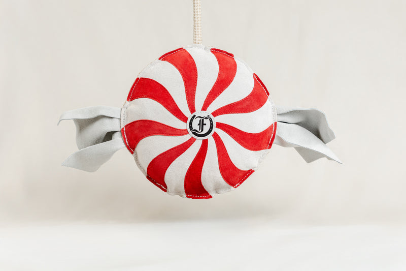Red-and-white peppermint swirl horse toy with fabric ends and a rope handle, featuring the Freedman logo at the center, displayed against a beige background."
