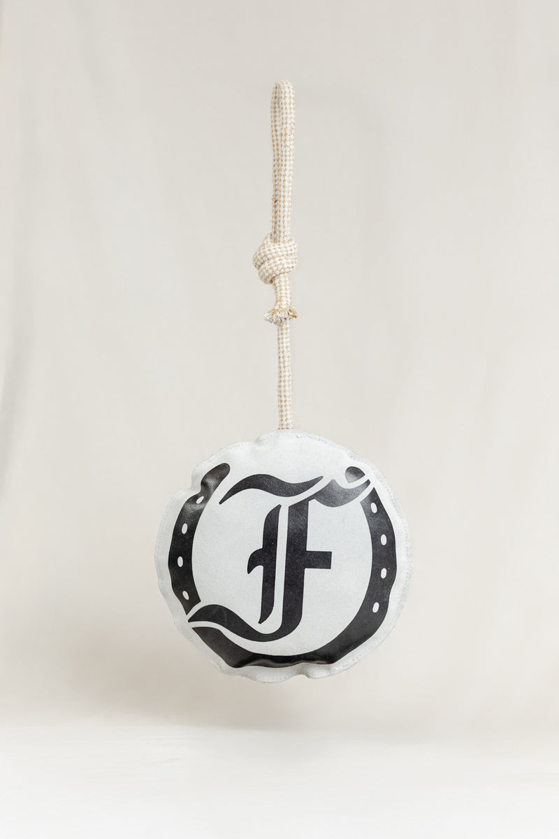 Round horse toy featuring the black Freedman logo and horseshoe graphic, hanging from a knotted rope on a light beige background