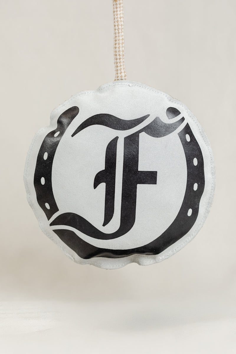 Round horse toy featuring the black Freedman logo and horseshoe graphic, hanging from a knotted rope on a light beige background
