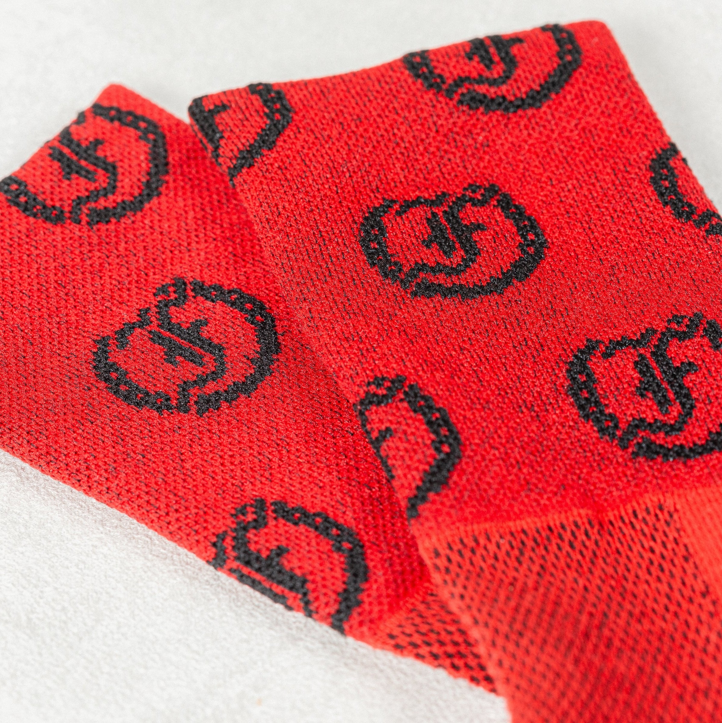 Close-up of red socks with repeating black circular Freedman's logo pattern, showing distinct knit texture and fabric details, light textured background.