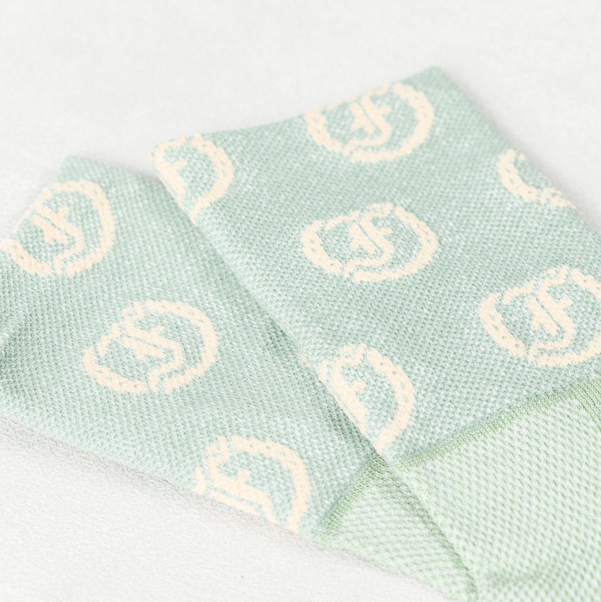 Close-up of light green socks with repeating light circular Freedman's logo pattern, showing distinct knit texture and fabric details, light textured background.