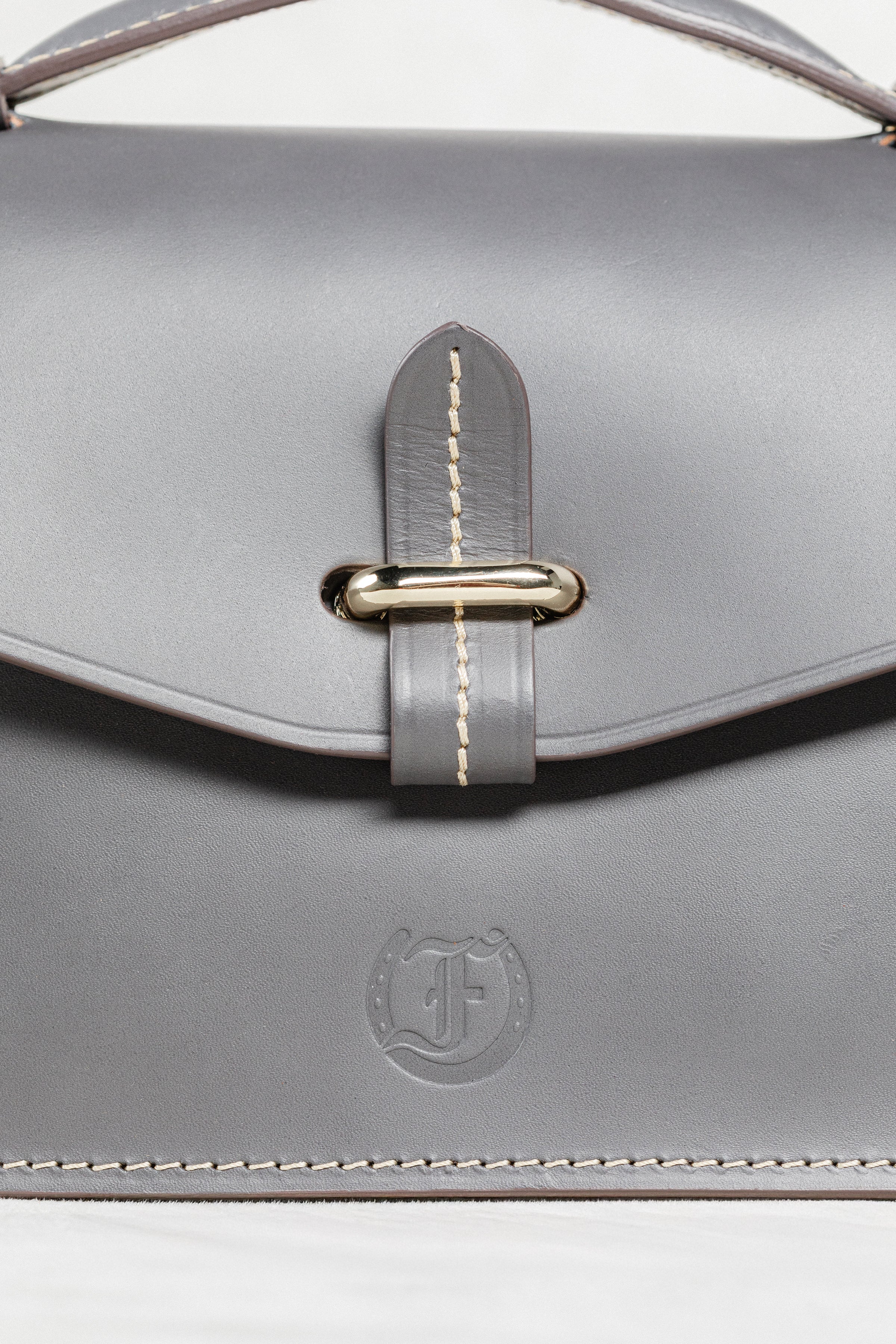 Close-up of grey leather Mantelet Bag by Freedman's, highlighting gold-tone slide lock, contrasting stitching, and embossed brand logo.