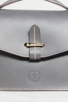 Close-up of grey leather Mantelet Bag by Freedman's, highlighting gold-tone slide lock, contrasting stitching, and embossed brand logo.