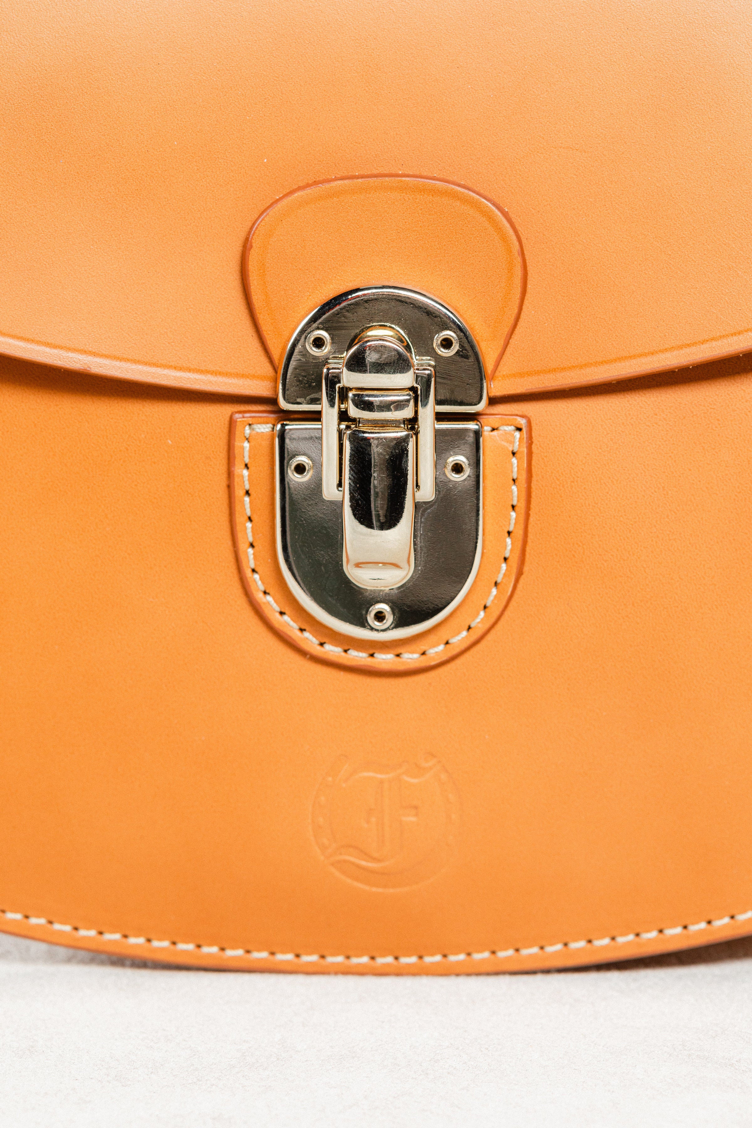 Close-up of cognac leather Minibus Bag by Freedman's, highlighting gold-tone turn-lock closure and embossed brand logo.