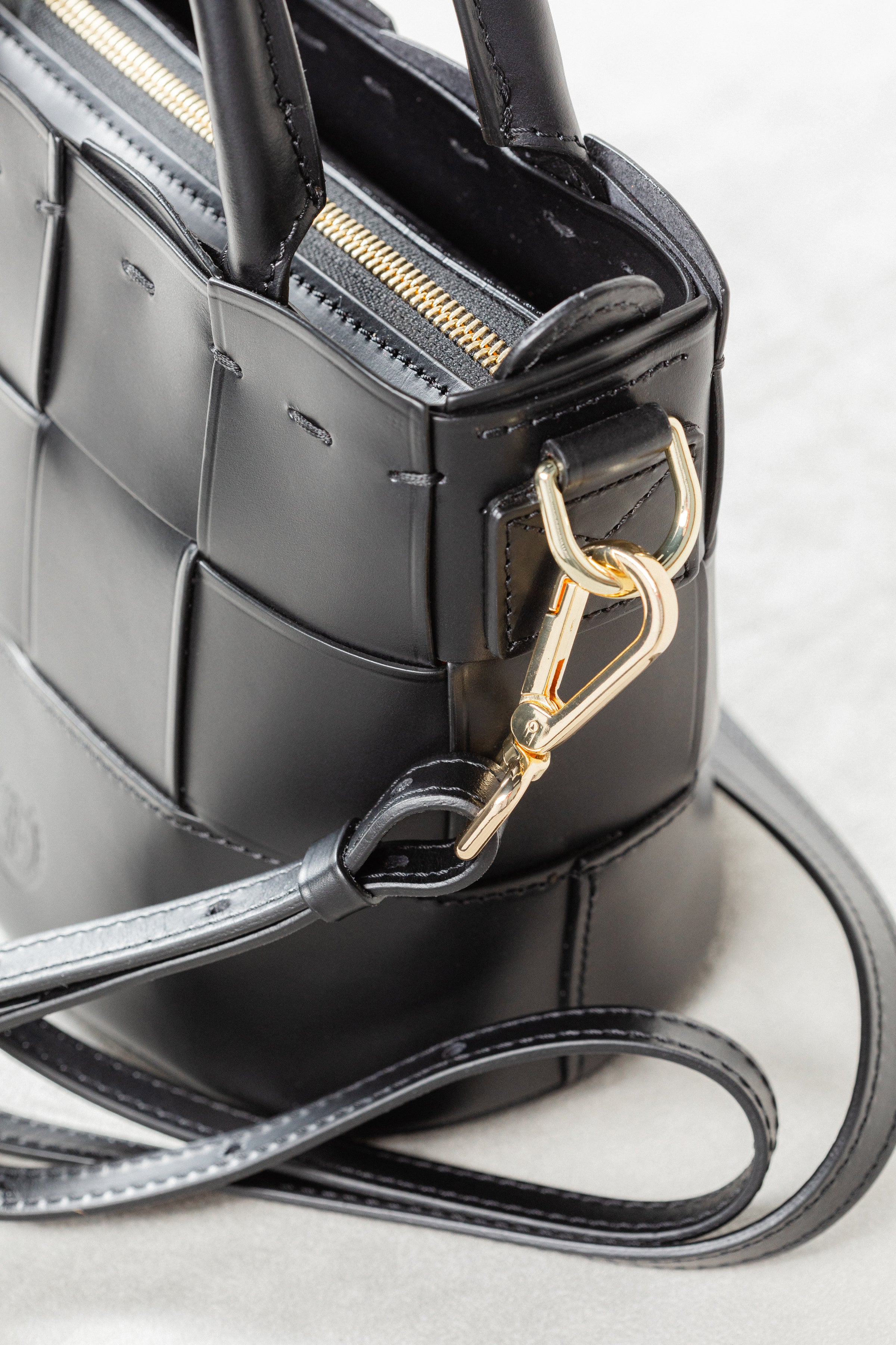 Close-up of black leather Milord Bag by Freedman's, highlighting gold-tone clasp hardware and adjustable strap attachment.